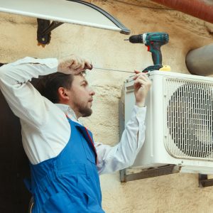 HVAC technician working on a capacitor part for condensing unit. Male worker or repairman in uniform repairing and adjusting conditioning system, diagnosting and looking for technical issues.